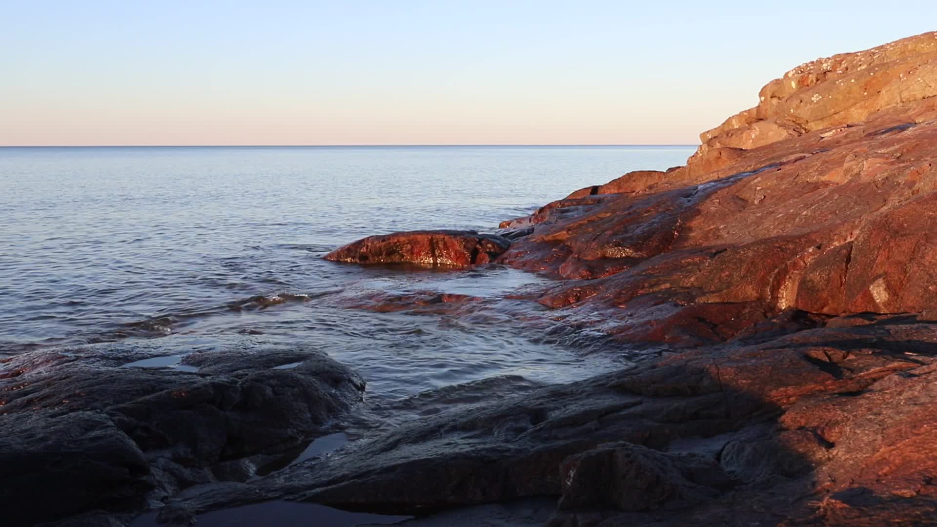 Lake Superior shoreline in early morning, flat water against red rock